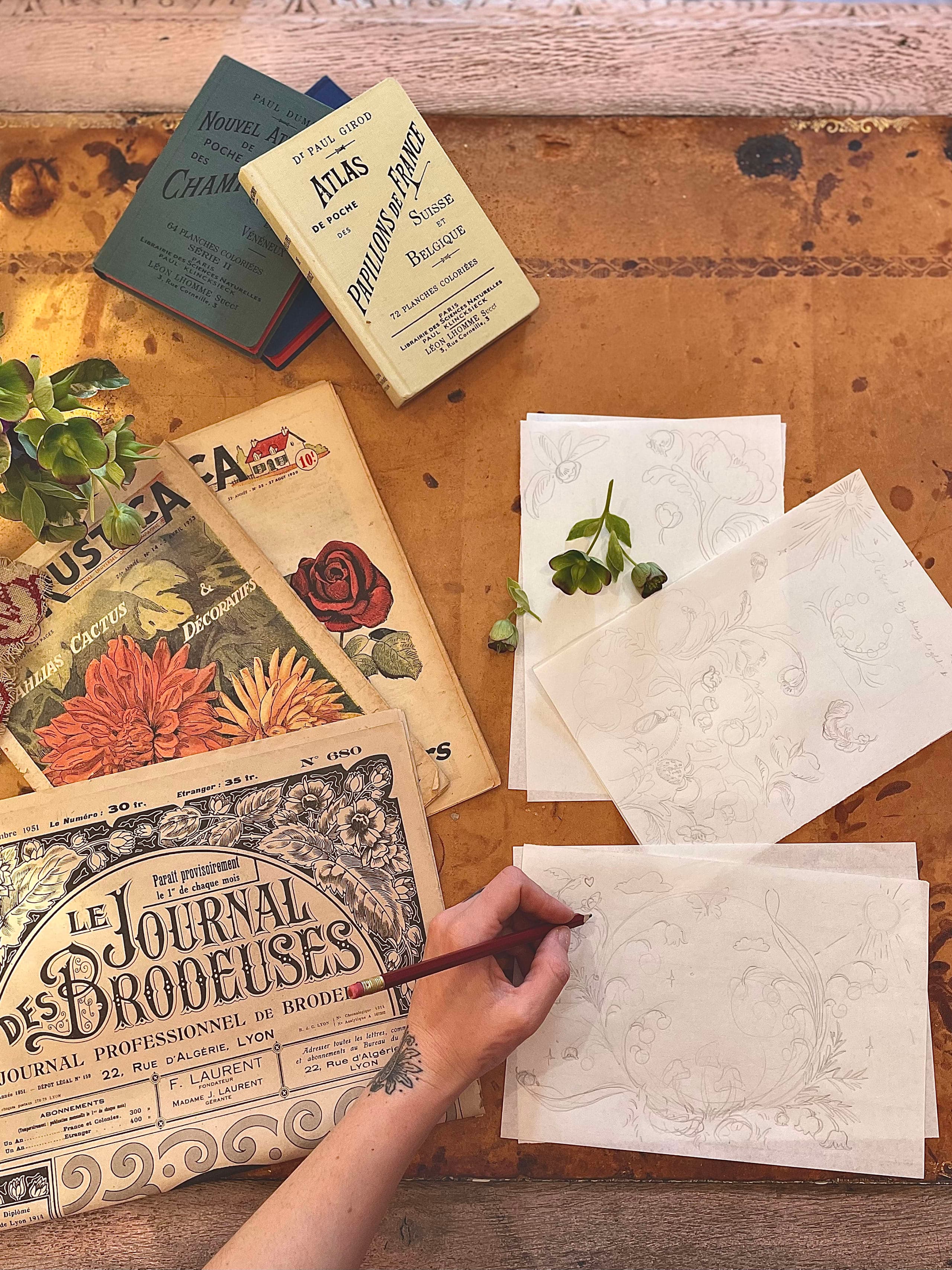 散らばった作業用紙の上でペンを持ちながらドローイングしているアーティスト